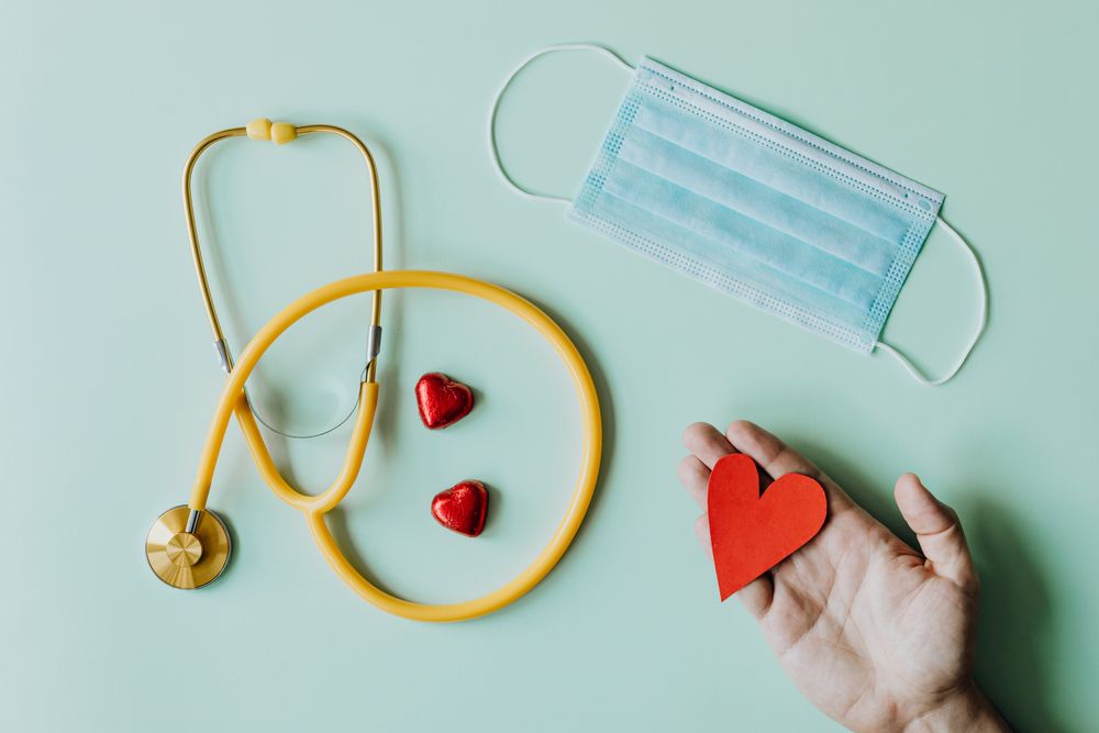 A stethoscope, a mask, and a paper heart on a pale table